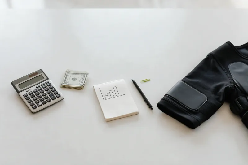 A calculator, dollar bills and a notepad beside the sleeve of an EMS suit